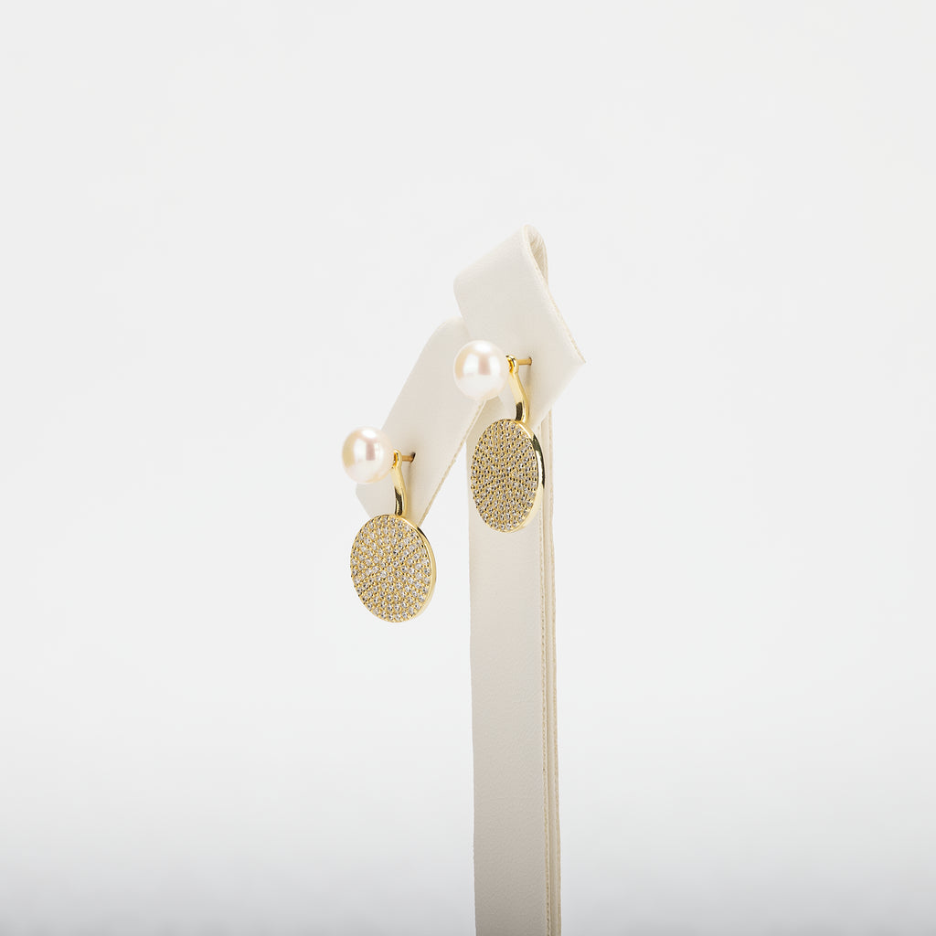 Pearl earrings with circular designs on a white stand against a white background