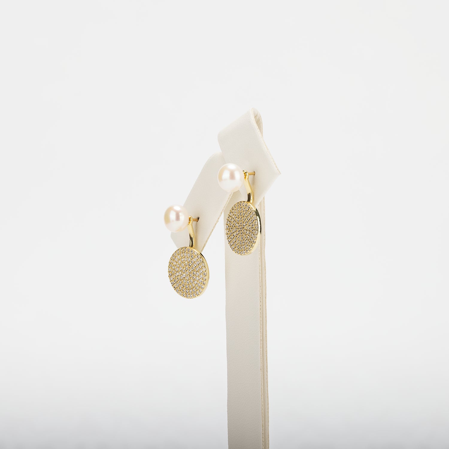 Pearl earrings with circular designs on a white stand against a white background